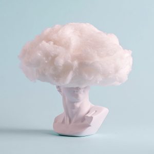 Fun still life if a white Grecian bust with woolly hat, hairdo or head covering cloud over a pale blue background